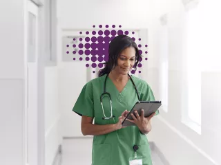 Healthcare professional walks down a hallway looking at a tablet